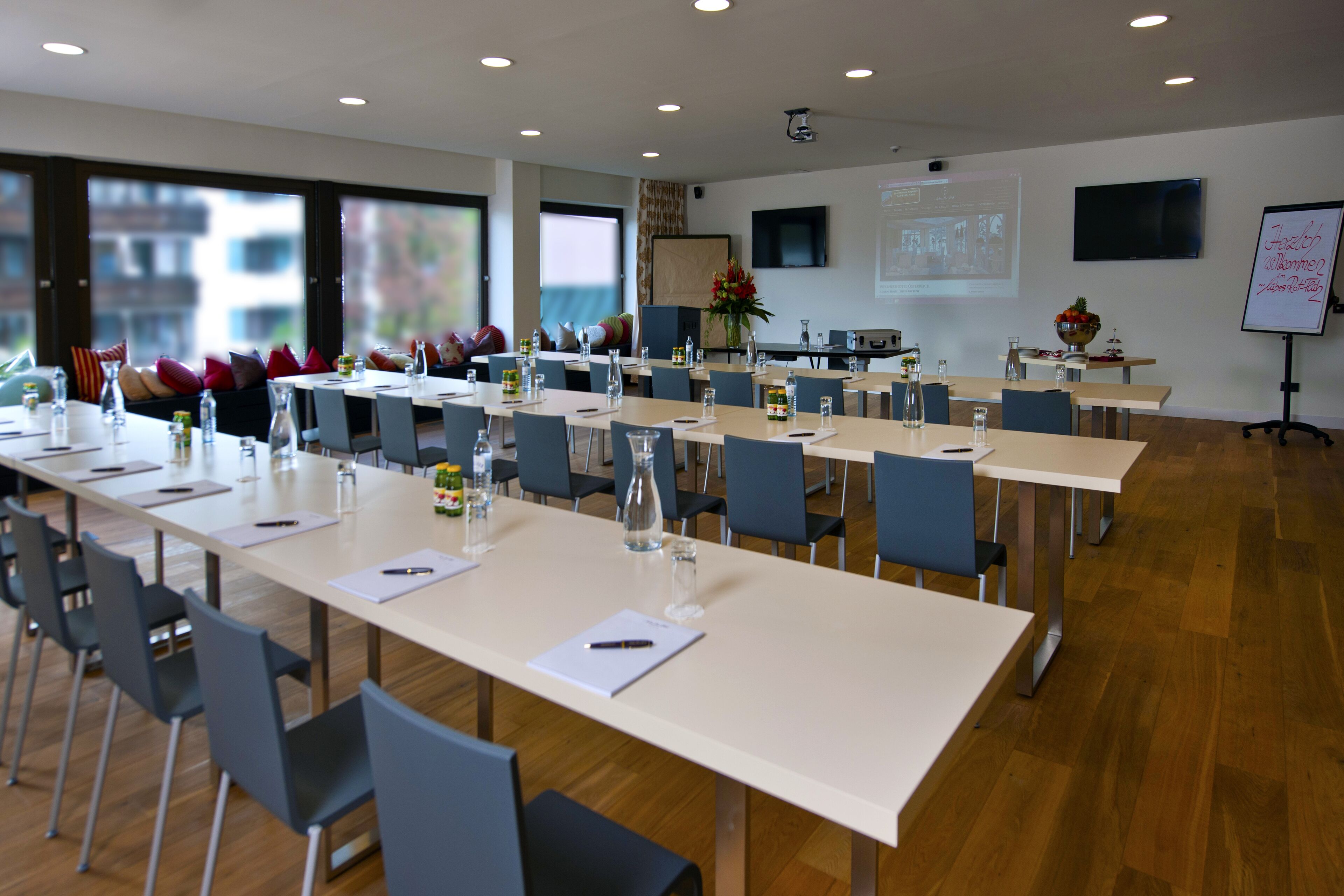 Ein Konferenzraum mit langen Tischen, Stühlen und einer Projektionsleinwand.