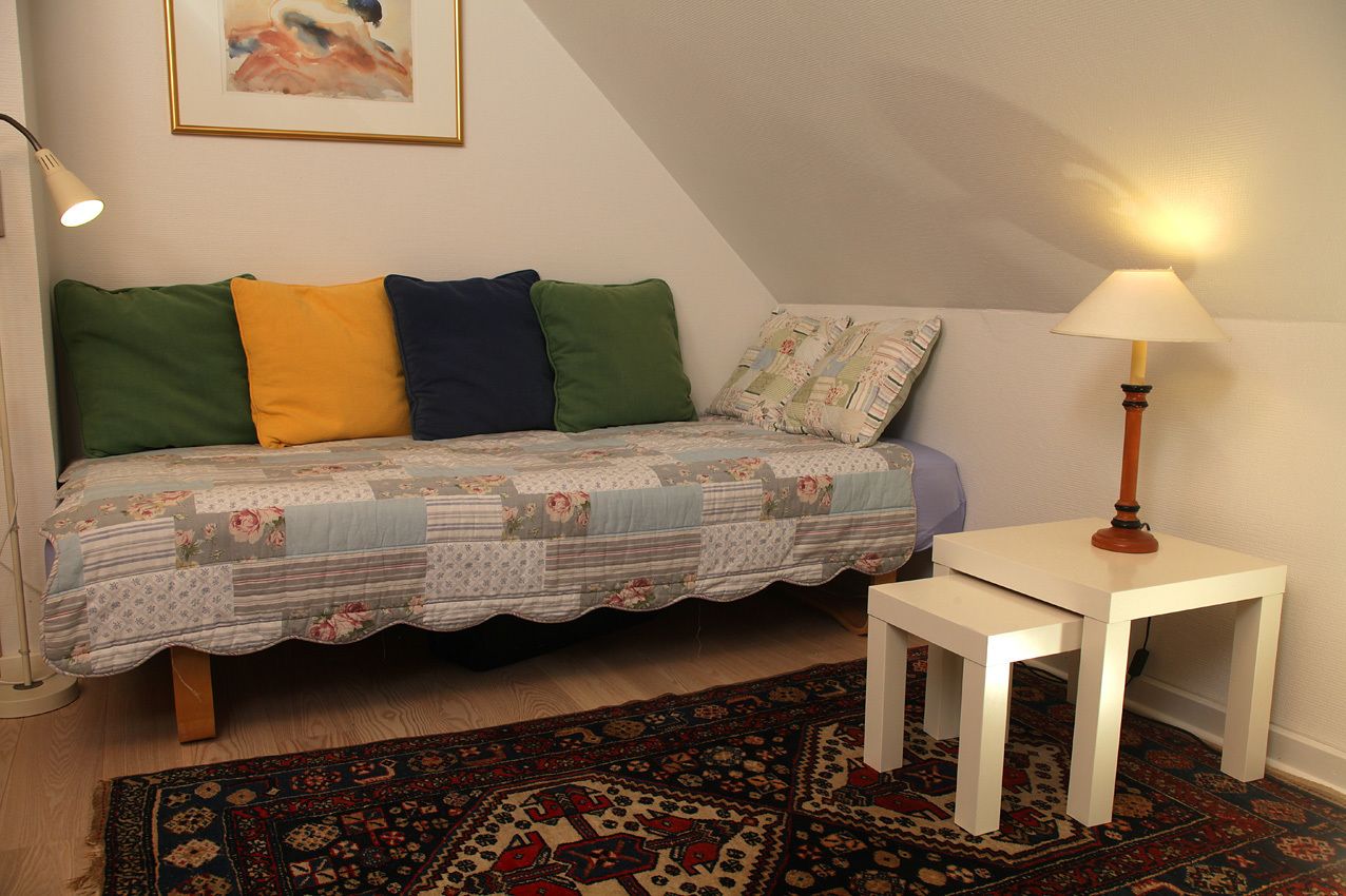 Ein gemütliches Zimmer mit einem Bett, einem kleinen weißen Tisch, einer Lampe und einem gemusterten Teppich.