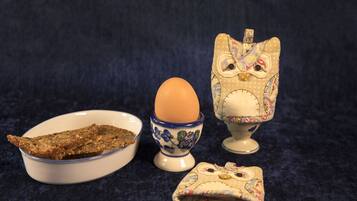 Un bol de pescado frito, una taza para huevos de cerámica y un recipiente decorativo con forma de lechuza.