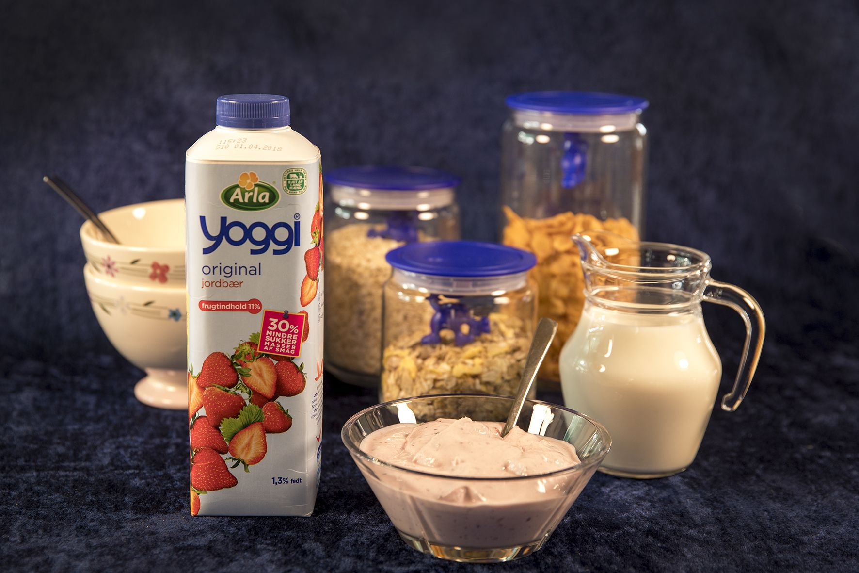 A carton of Arla Yoggj milk, a bowl of yogurt, a glass of milk, and jars of granola and honey.