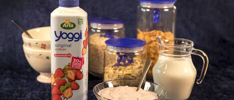 A carton of Arla Yoggj milk, a bowl of yogurt, a glass of milk, and jars of granola and honey.