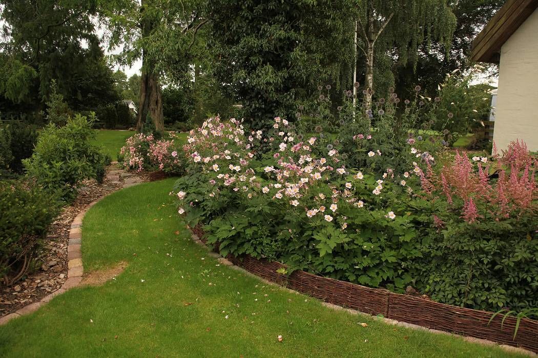 Un jardín con un sendero curvo, abundante vegetación y plantas florecientes.