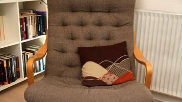 Una butaca con respaldo alto, asiento acolchado y reposabrazos, ubicada frente a una estantería llena de libros.