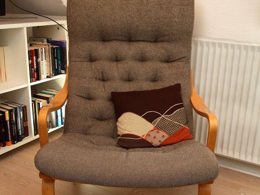 Una butaca con respaldo alto, asiento acolchado y reposabrazos, ubicada frente a una estantería llena de libros.