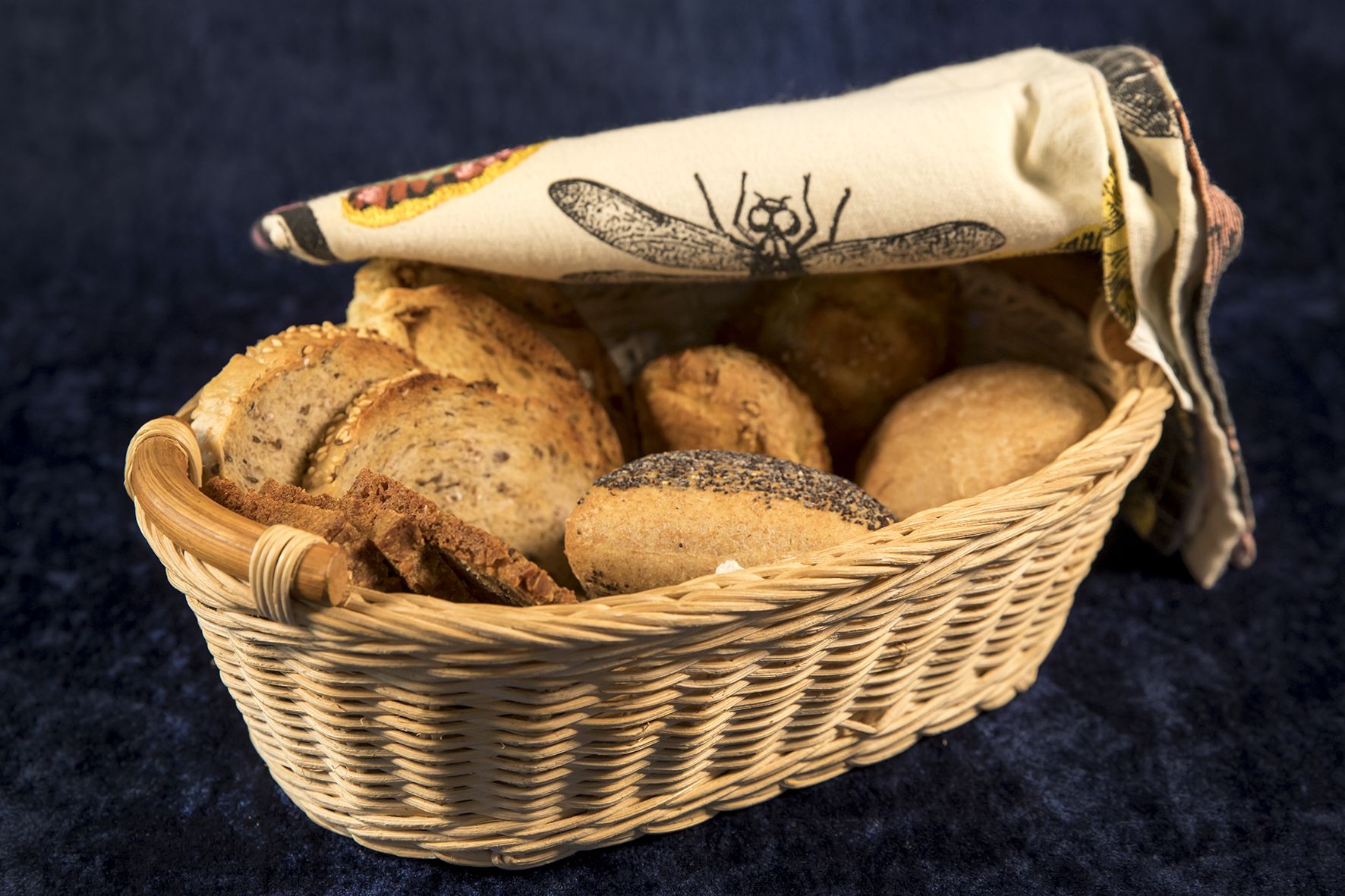 A wicker basket filled with various types of bread, including sliced and whole loaves, placed on a dark surface.