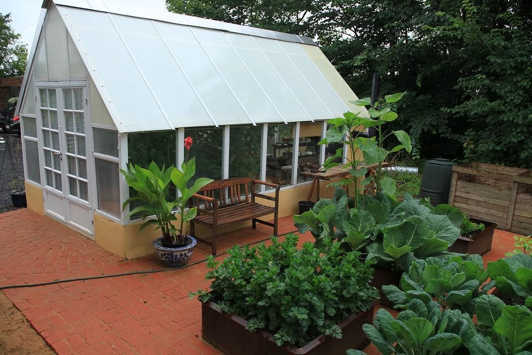 A greenhouse with a sloped roof, a bench, and potted plants.