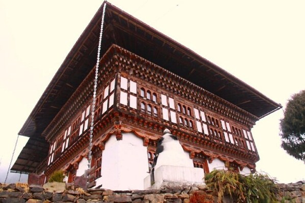 A traditional building with a steeply pitched roof, wooden lattice detailing, and a white base. - Thegchen Phodrang Lodge (Wangdue Phodrang)