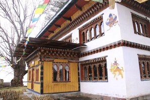 A traditional building with ornate wooden carvings and colorful flags. - Thegchen Phodrang Lodge (Wangdue Phodrang)