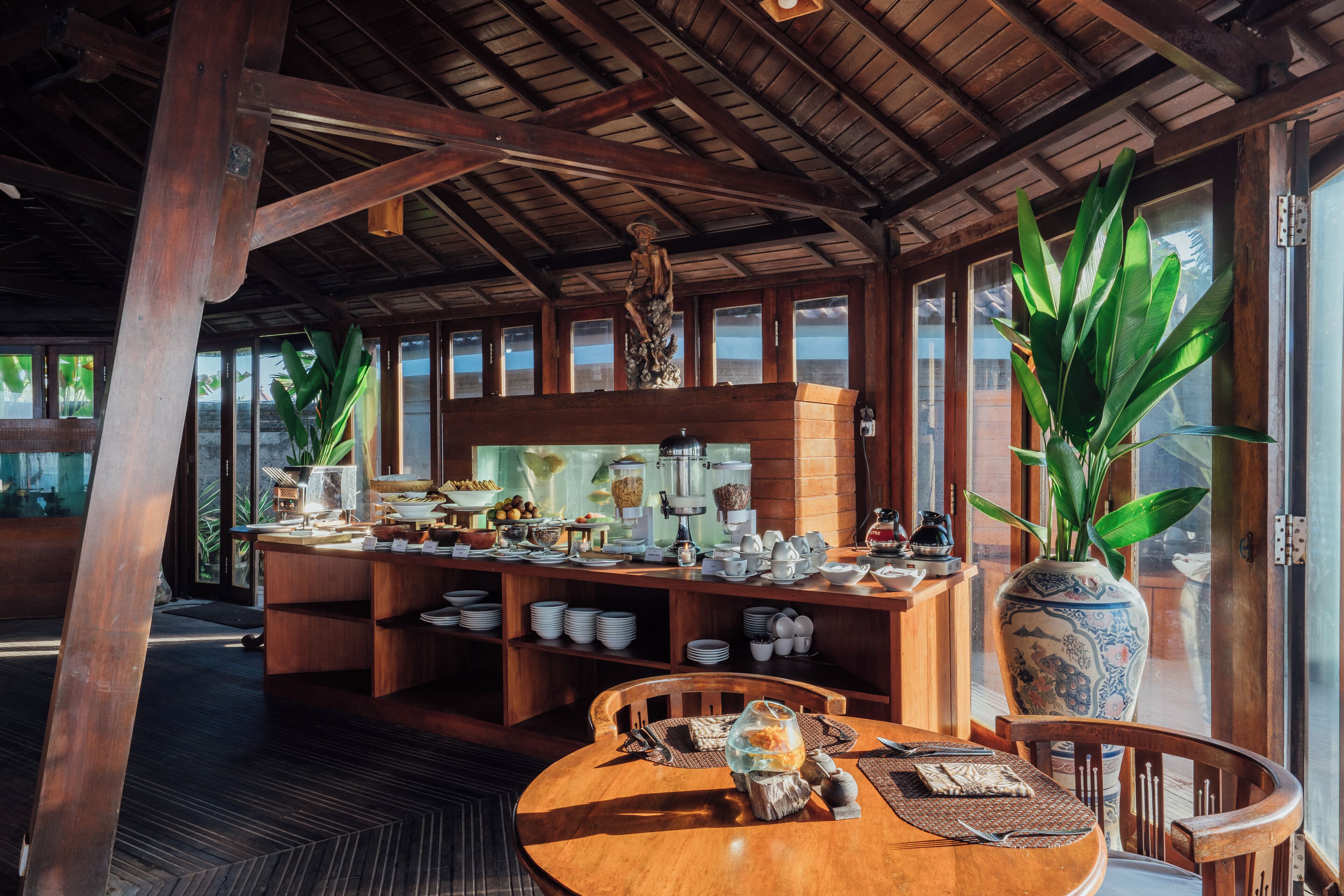 A wooden dining area with a buffet setup, large windows, and a decorative vase.