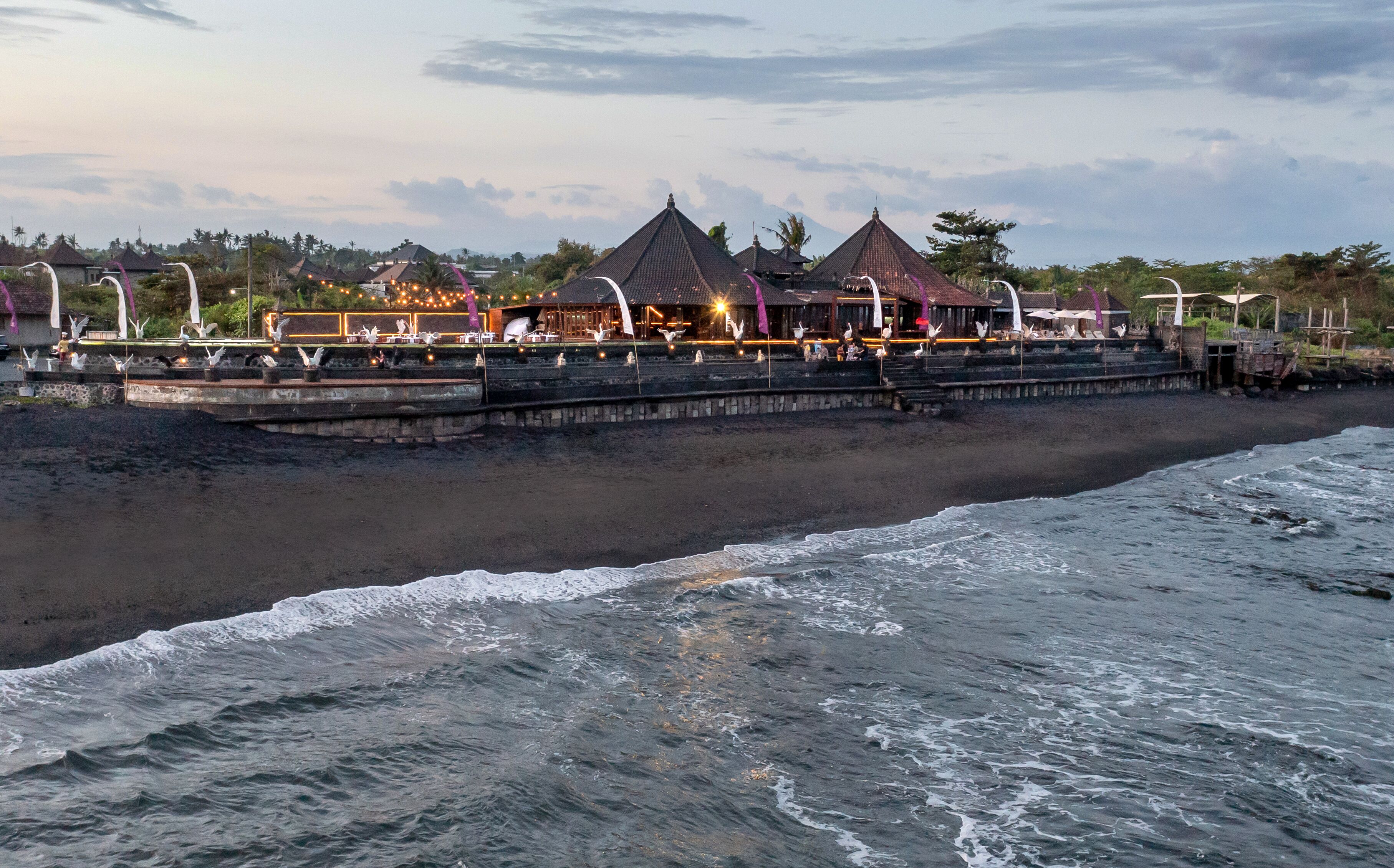 A beachfront resort with thatched-roof buildings, a pier, and a view of the ocean.