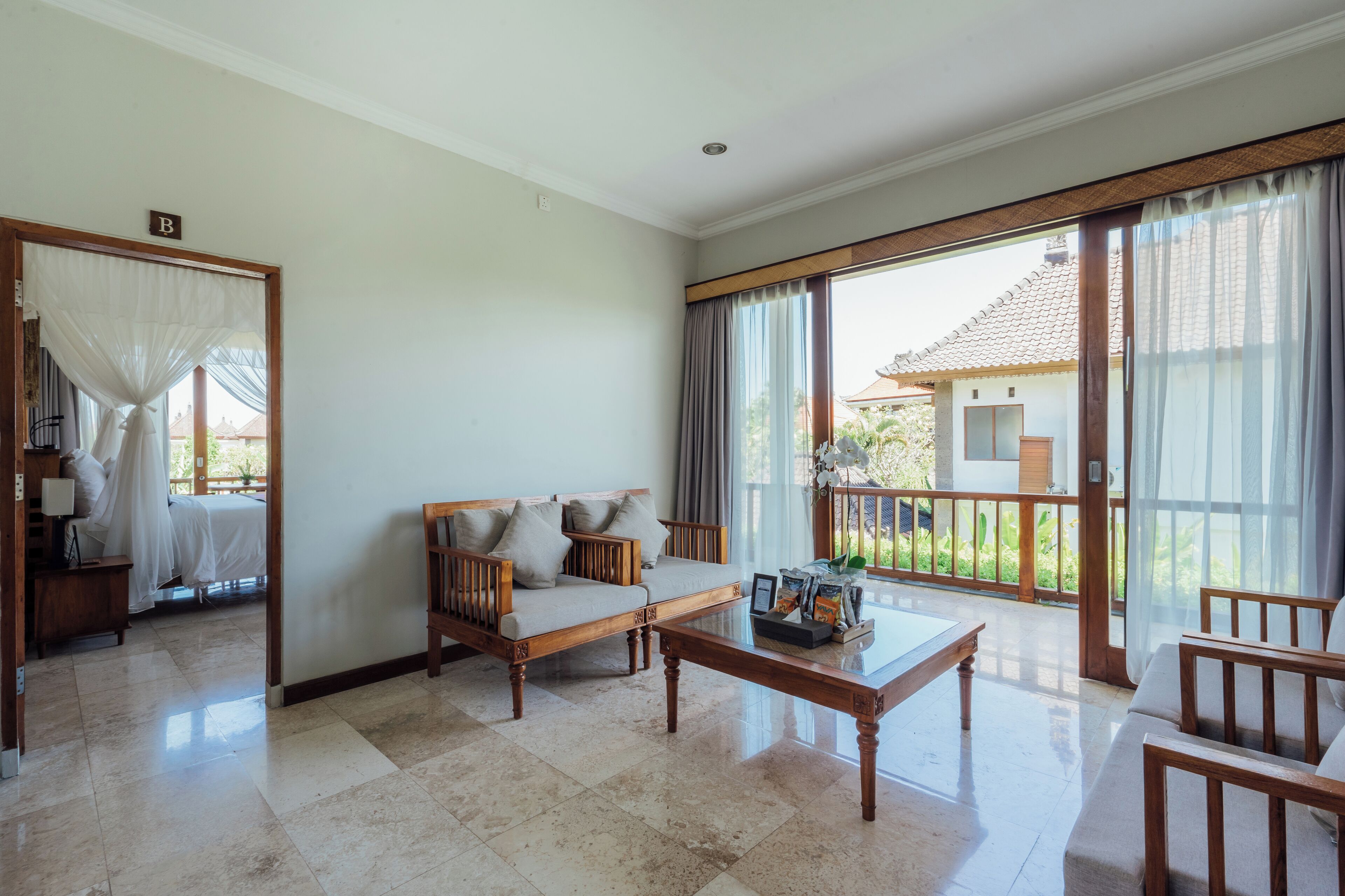 A spacious living area with a sofa, coffee table, and a balcony with curtains.