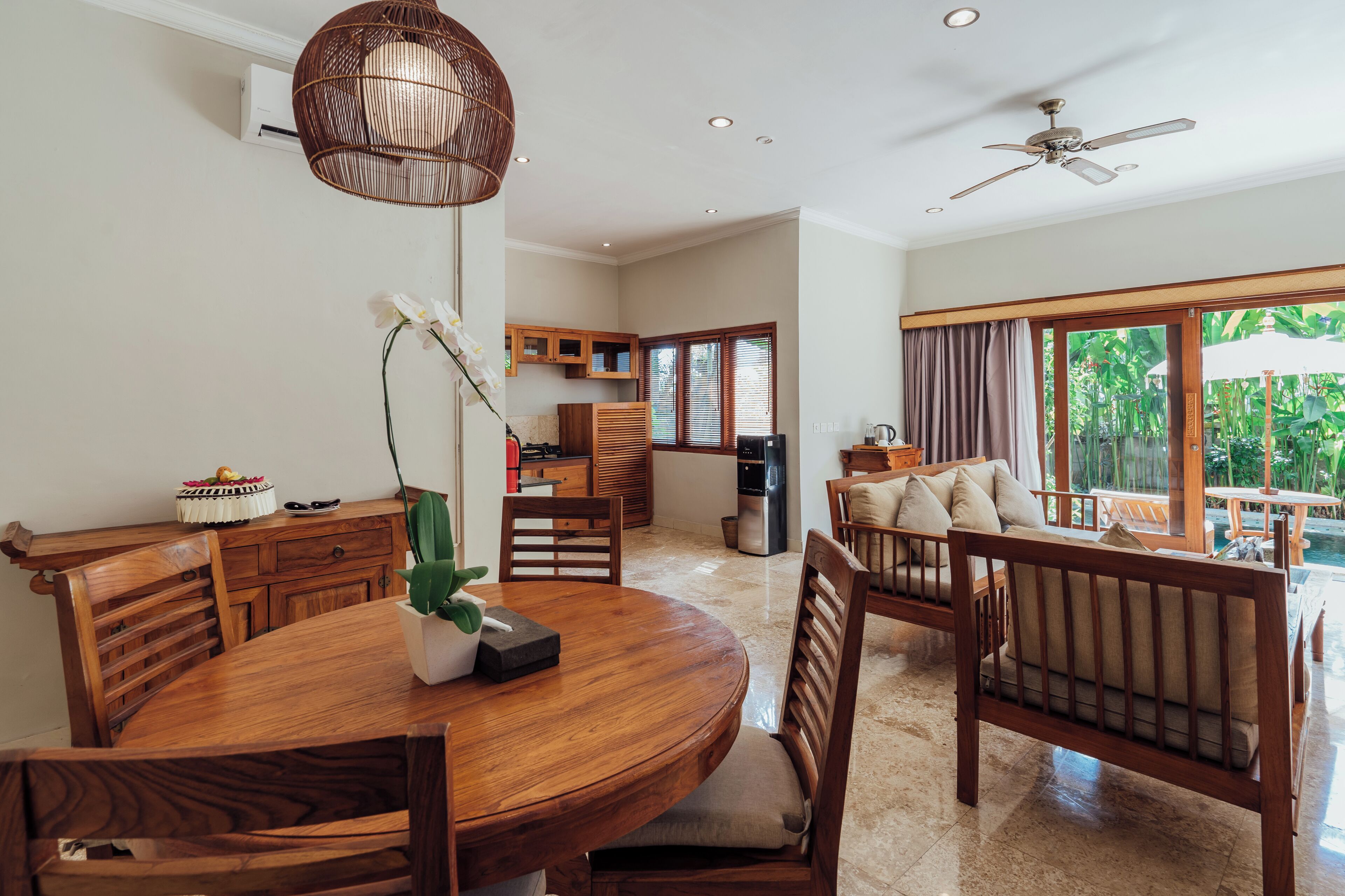 A modern dining area with a wooden table and chairs, a hanging light fixture, and a view of the outdoor patio.