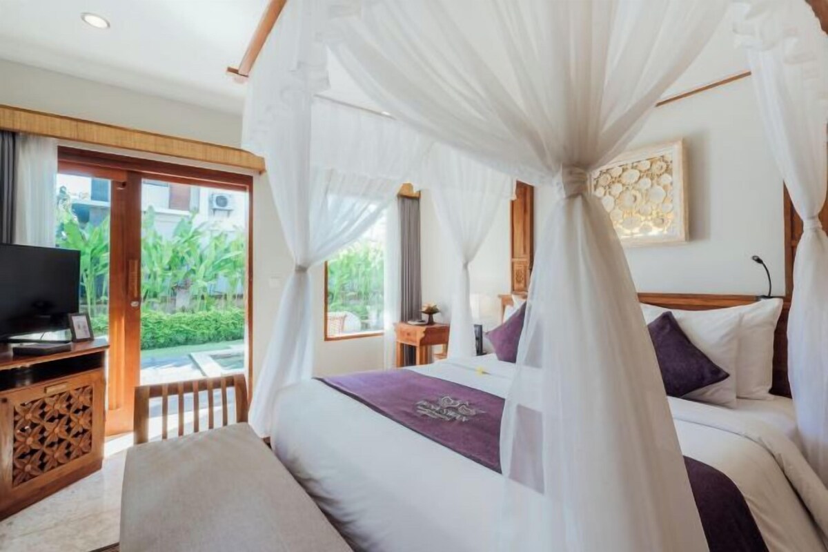 A bedroom with a bed, a television, a wooden cabinet, and a view of greenery outside.