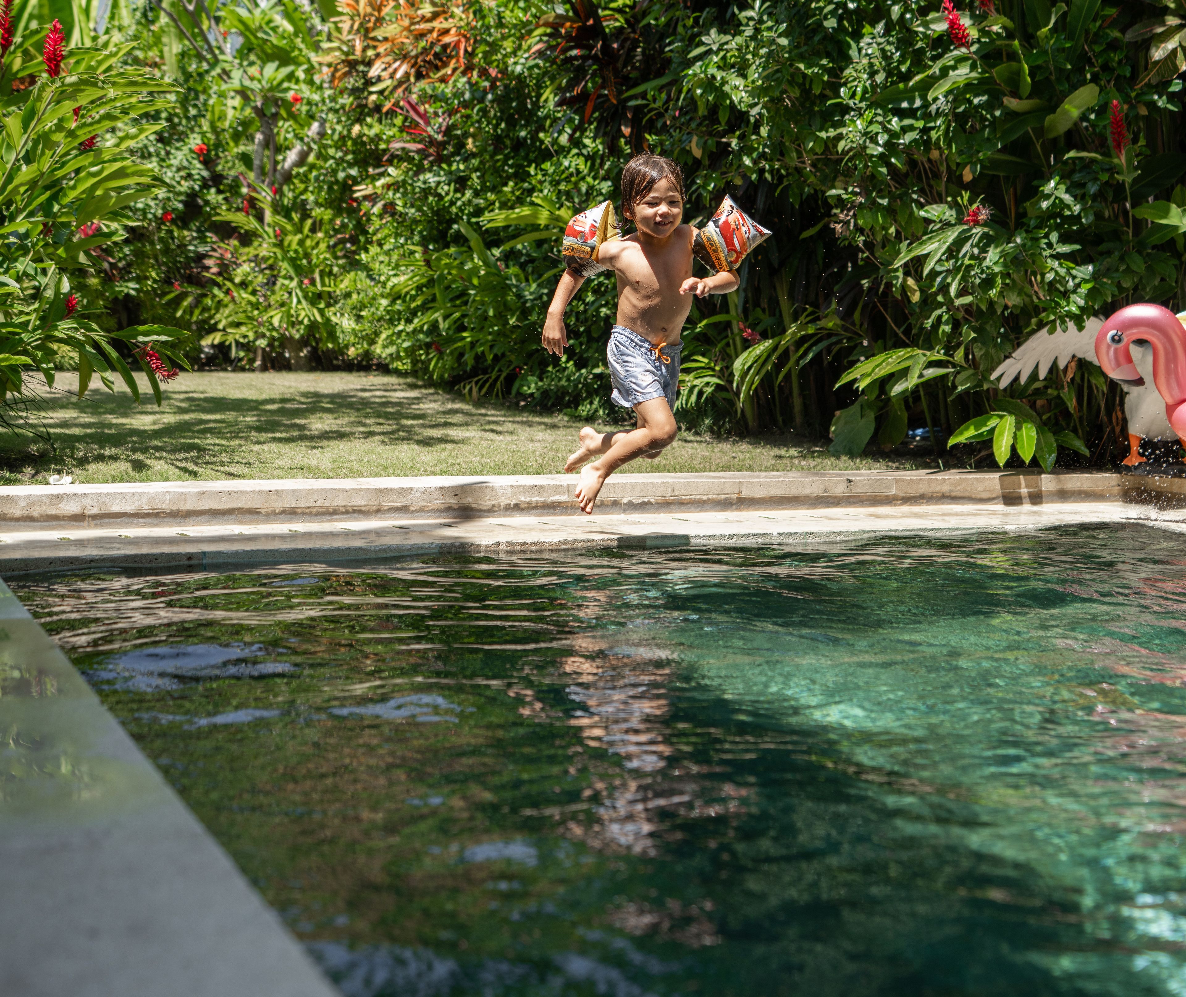 A person jumping into a swimming pool with a flamingo float.