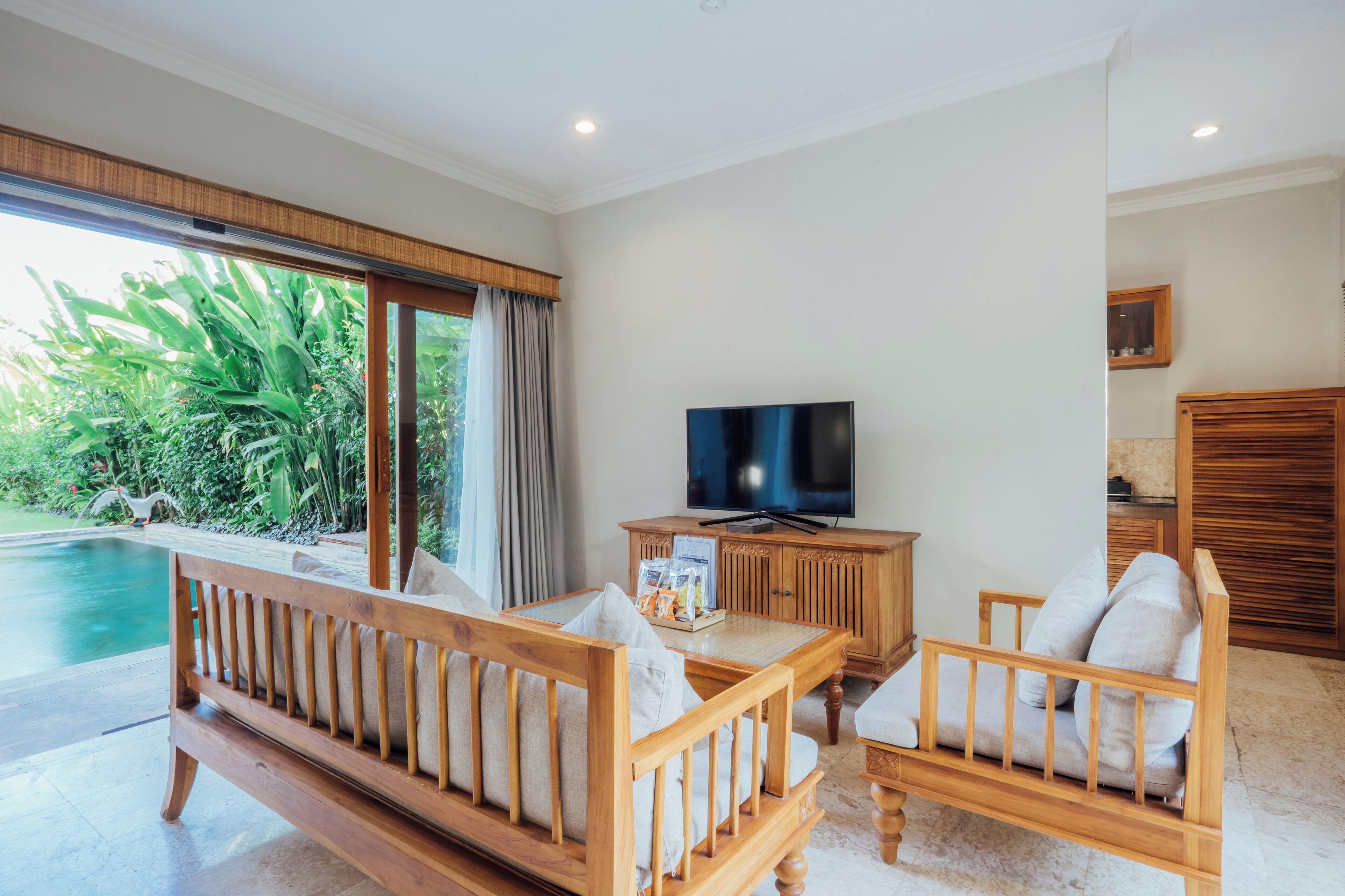 A spacious living area with a wooden sofa, a television, and a view of a swimming pool.