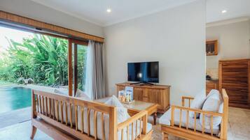 A spacious living area with a wooden sofa, a television, and a view of a swimming pool.