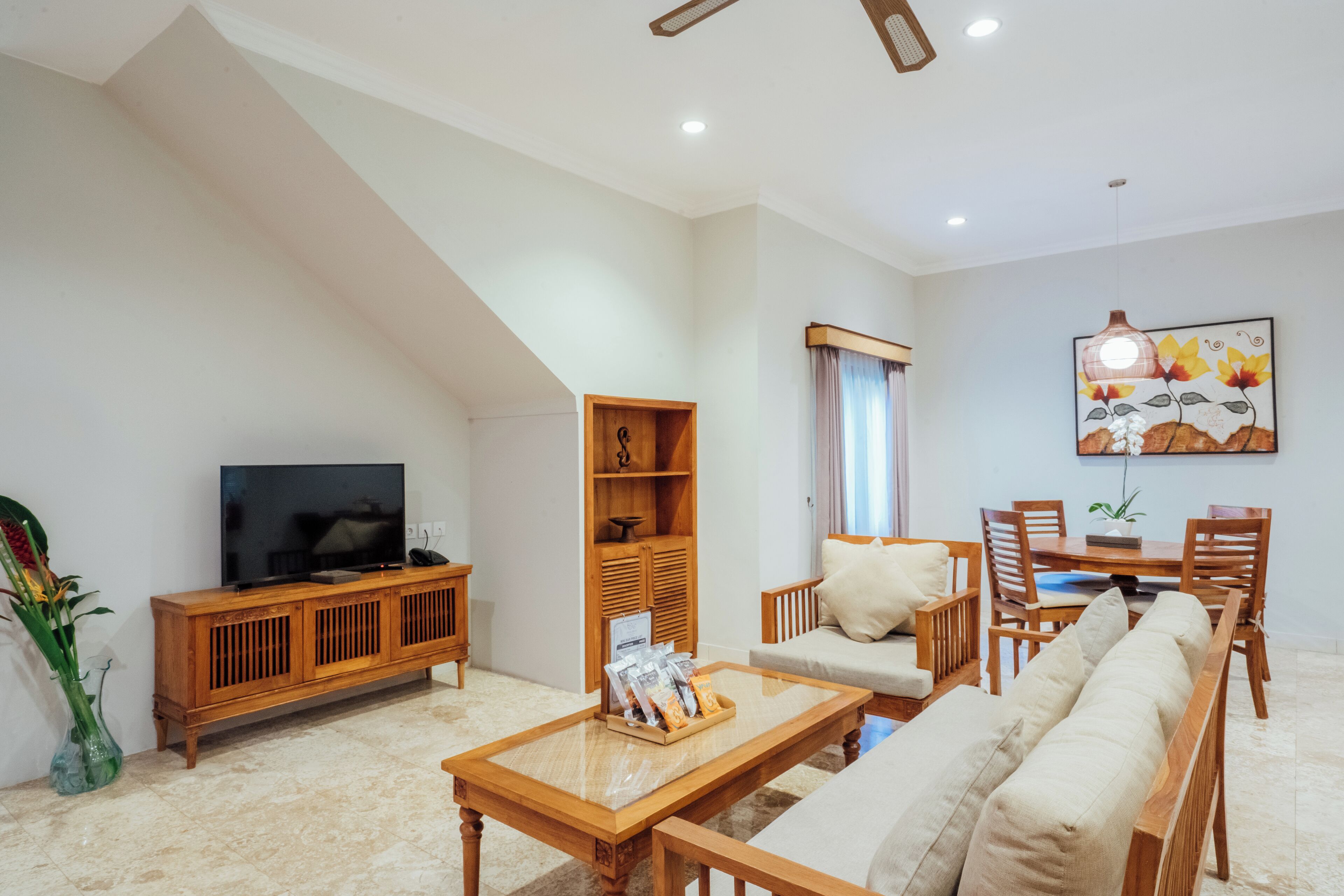 Una sala de estar con televisor, muebles de madera, una estantería y un comedor con sillas y una mesa.