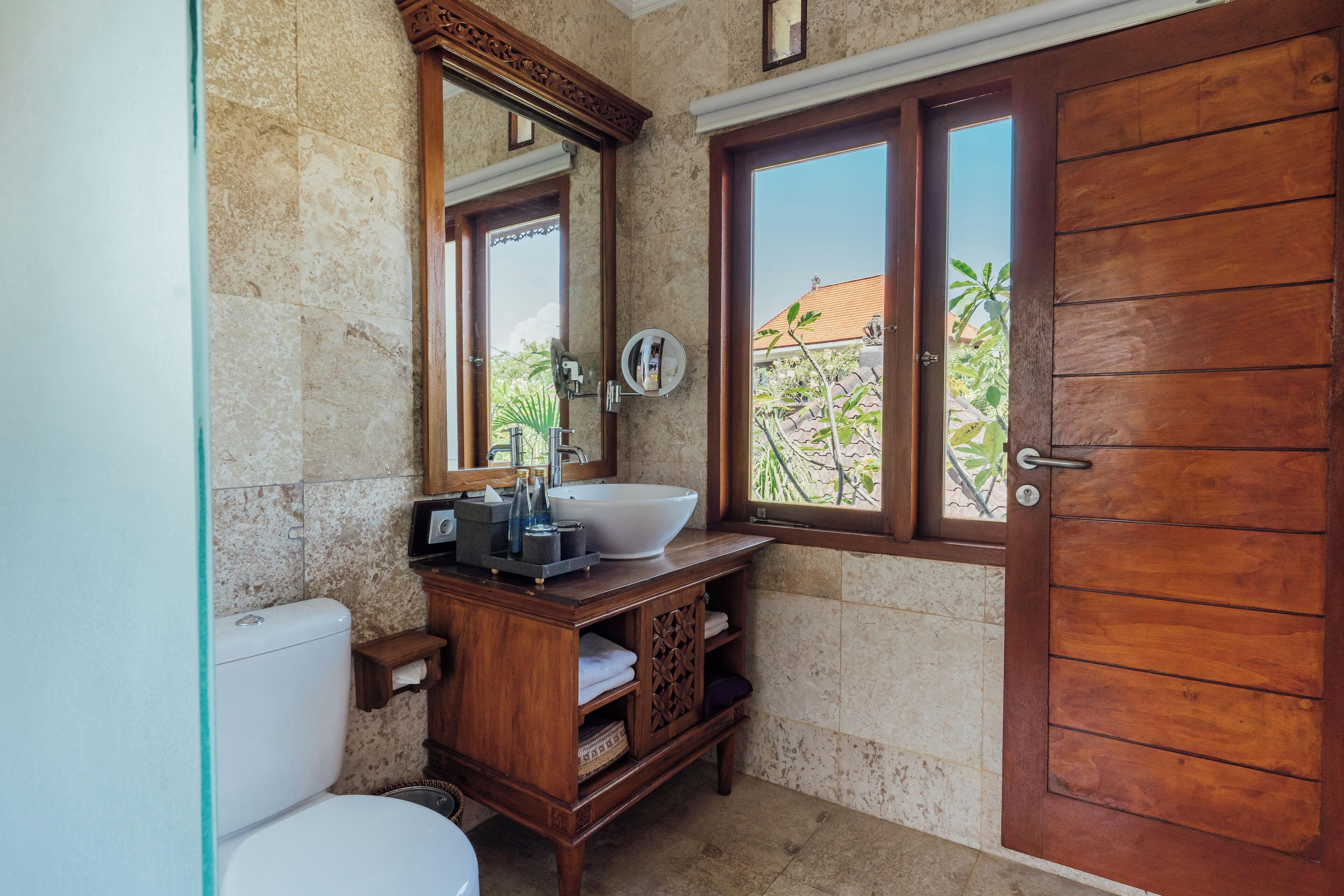 A bathroom with a wooden vanity, a large mirror, a white sink, and a wooden door.