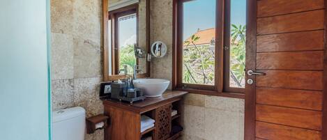 A bathroom with a wooden vanity, a large mirror, a white sink, and a wooden door.