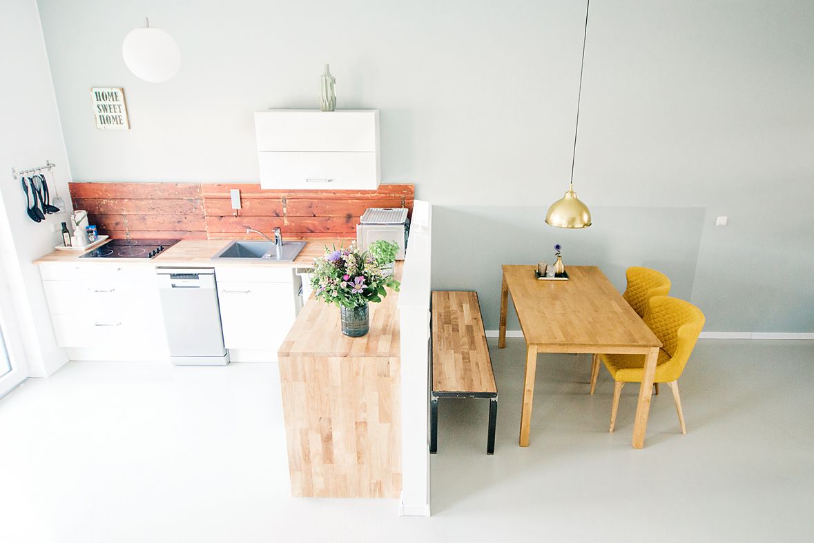 A modern kitchen with white cabinets, a wooden island, and a dining area with a wooden table and yellow chairs.