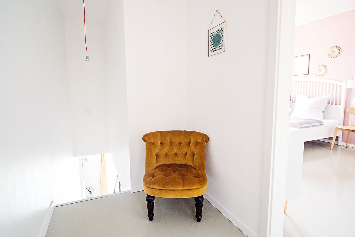 A corner room with a mustard-colored armchair, white walls, and a small decorative item on the wall.