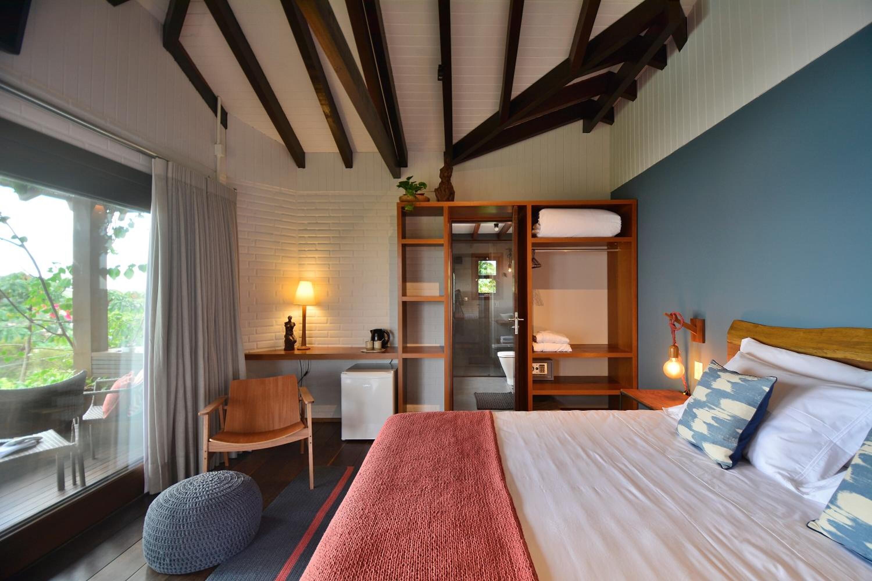 A bedroom with a bed, a desk, a chair, a small table, and a window with curtains.