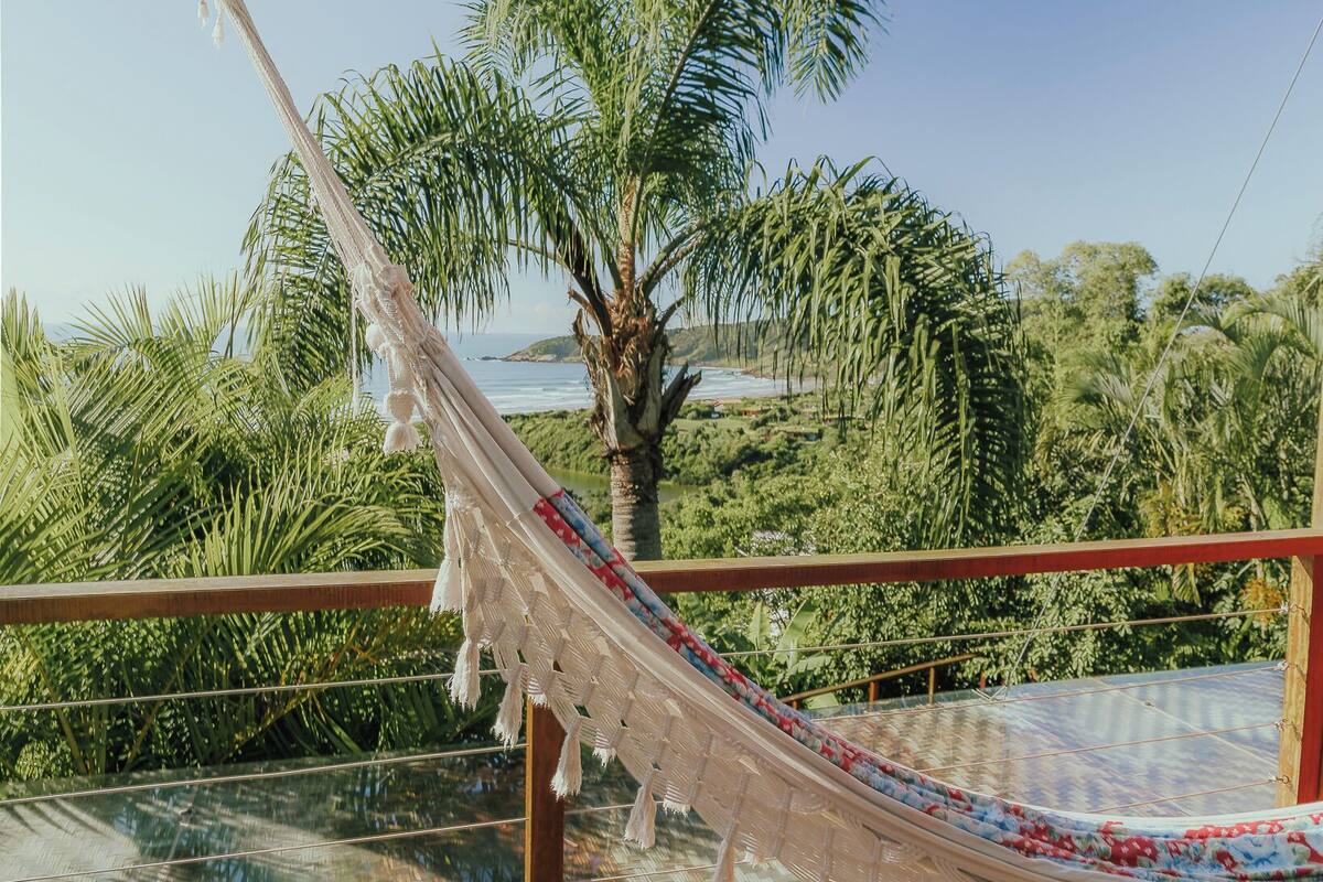 Eine Hängematte auf einer Holzterrasse mit Blick auf Palmen und einen Strand.