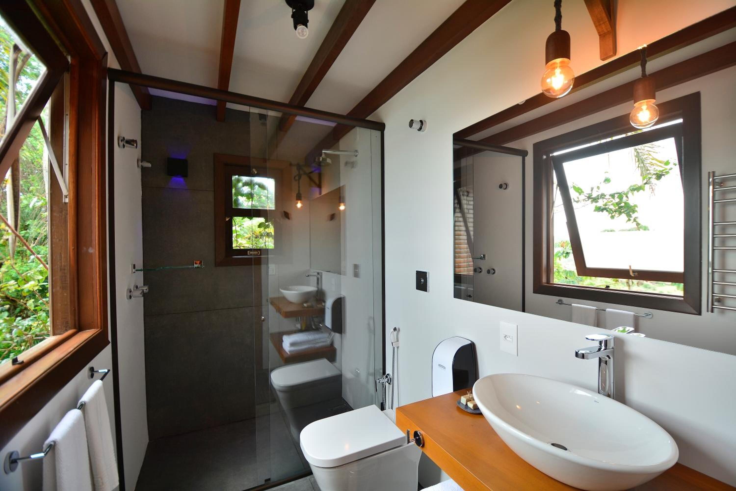 A modern bathroom with a glass shower enclosure, a white toilet, a wooden vanity with a large sink, and a mirror above the sink.