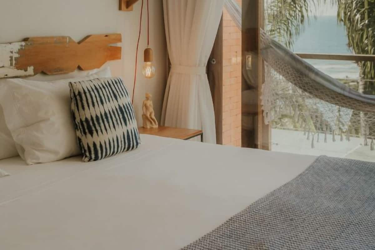 Ein Schlafzimmer mit einem großen Bett, einer Hängematte, Blick auf den Ozean und einem Holzkopfende.