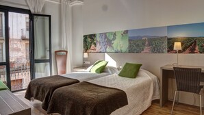 A hotel room with two beds, a desk, a chair, and a large window with a view of a vineyard. - Hostal Agrobotiga 7 de Ribera (Mora d'Ebre)