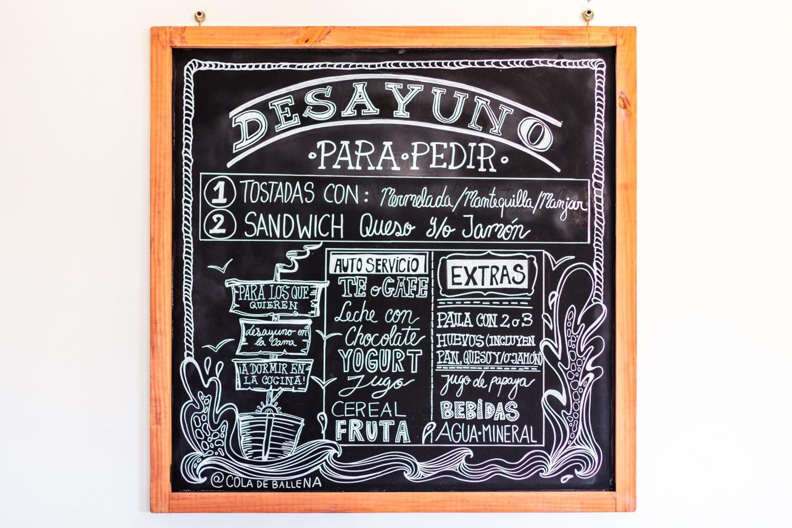 Un menú en pizarra con opciones de desayuno, incluyendo tostadas, sándwiches, yogur, cereales y fruta.