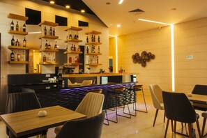 Un área de bar moderna con varios estantes para licores, una barra con taburetes y un comedor con mesas y sillas.