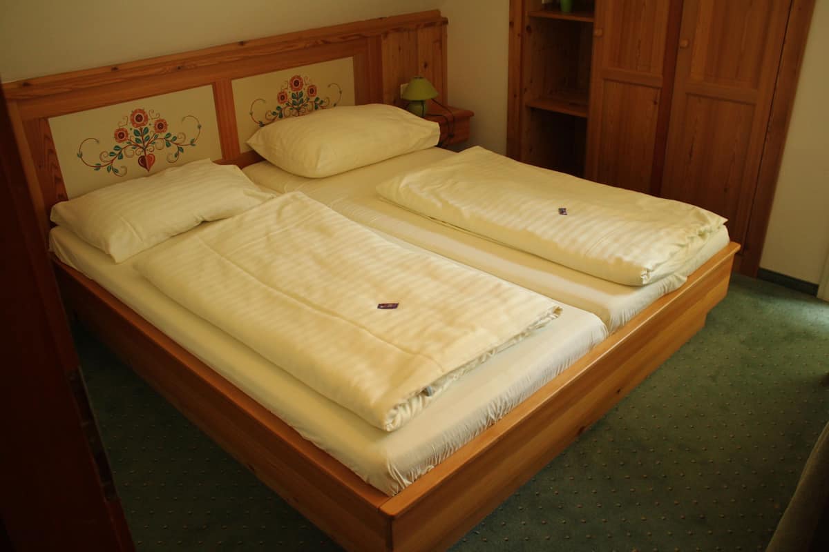 A double bed with wooden headboard and footboard, two pillows, and a bedside table with a lamp.