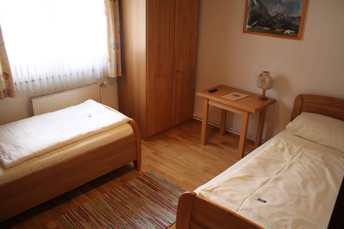 A bedroom with two single beds, a wooden wardrobe, a small table with a lamp, and a painting on the wall.