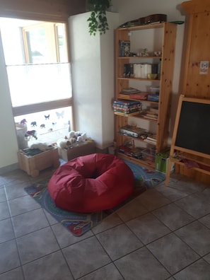 A room with a red bean bag chair, a bookshelf, a window with a view, and a chalkboard. - Pension Marienhof (Hermagor-Pressegger See)