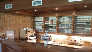 Un'area bar con un bancone in legno, sgabelli da bar e scaffali con bicchieri.