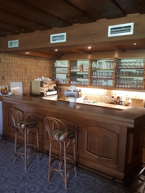 Zona de bar con mostrador de madera, taburetes y estanterías con cristalería.
