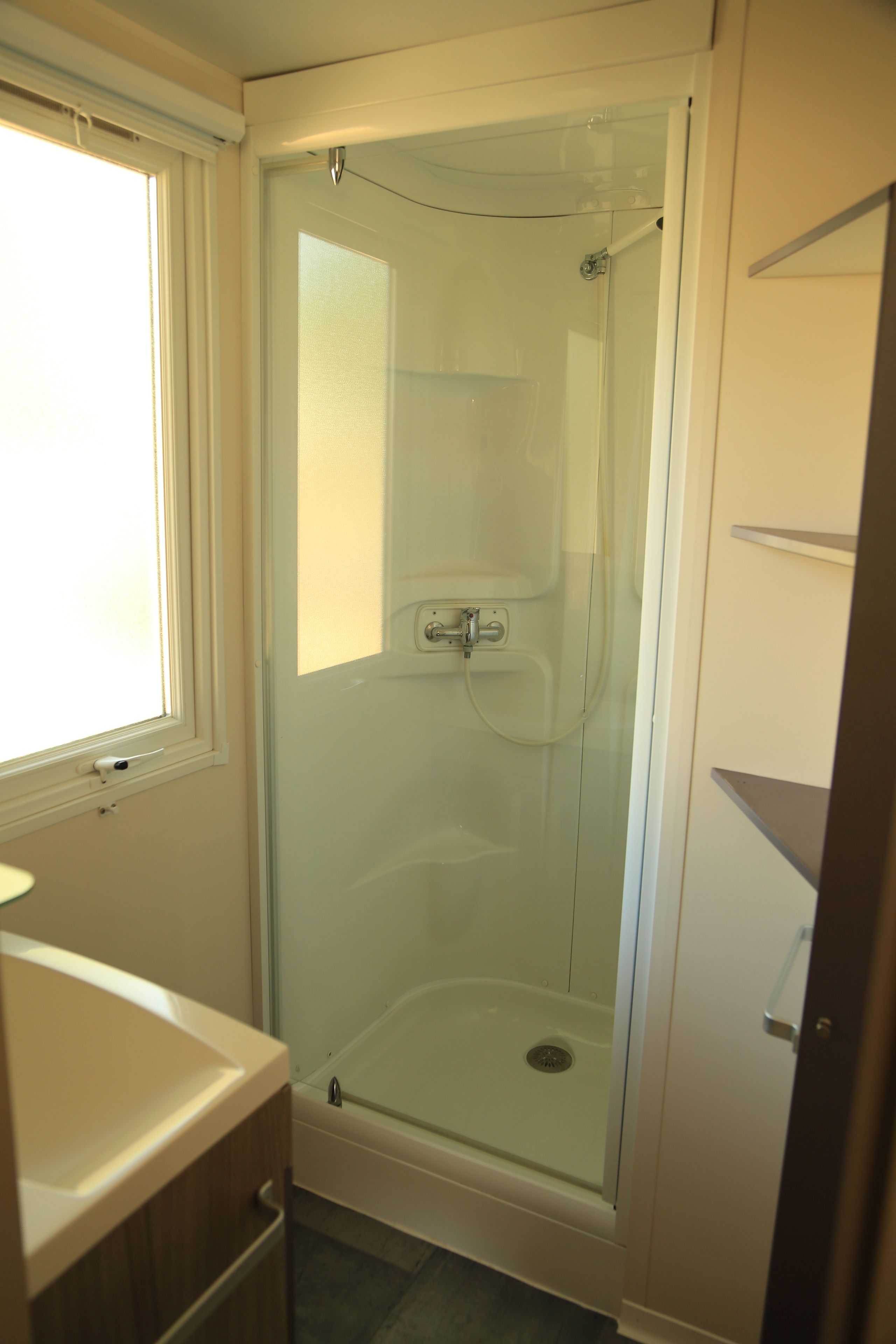 A bathroom with a glass-enclosed shower, a sink, and a window.