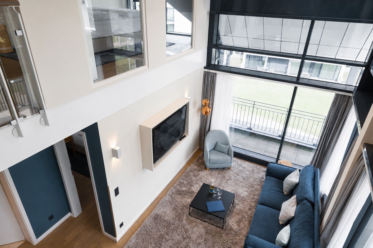 A modern living room with a sofa, a coffee table, a TV, and a balcony with a view.