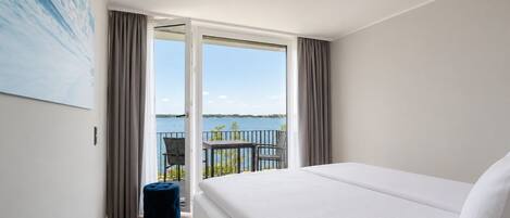 A hotel room with a bed, a view of the water, and a balcony with a table and chairs.