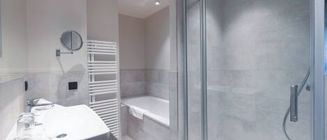 A modern bathroom with a glass-enclosed shower, a white bathtub, and a vanity with a mirror.