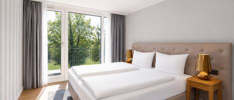 A hotel room with a large bed, two bedside tables, a ceiling light, and a view of greenery through the window.