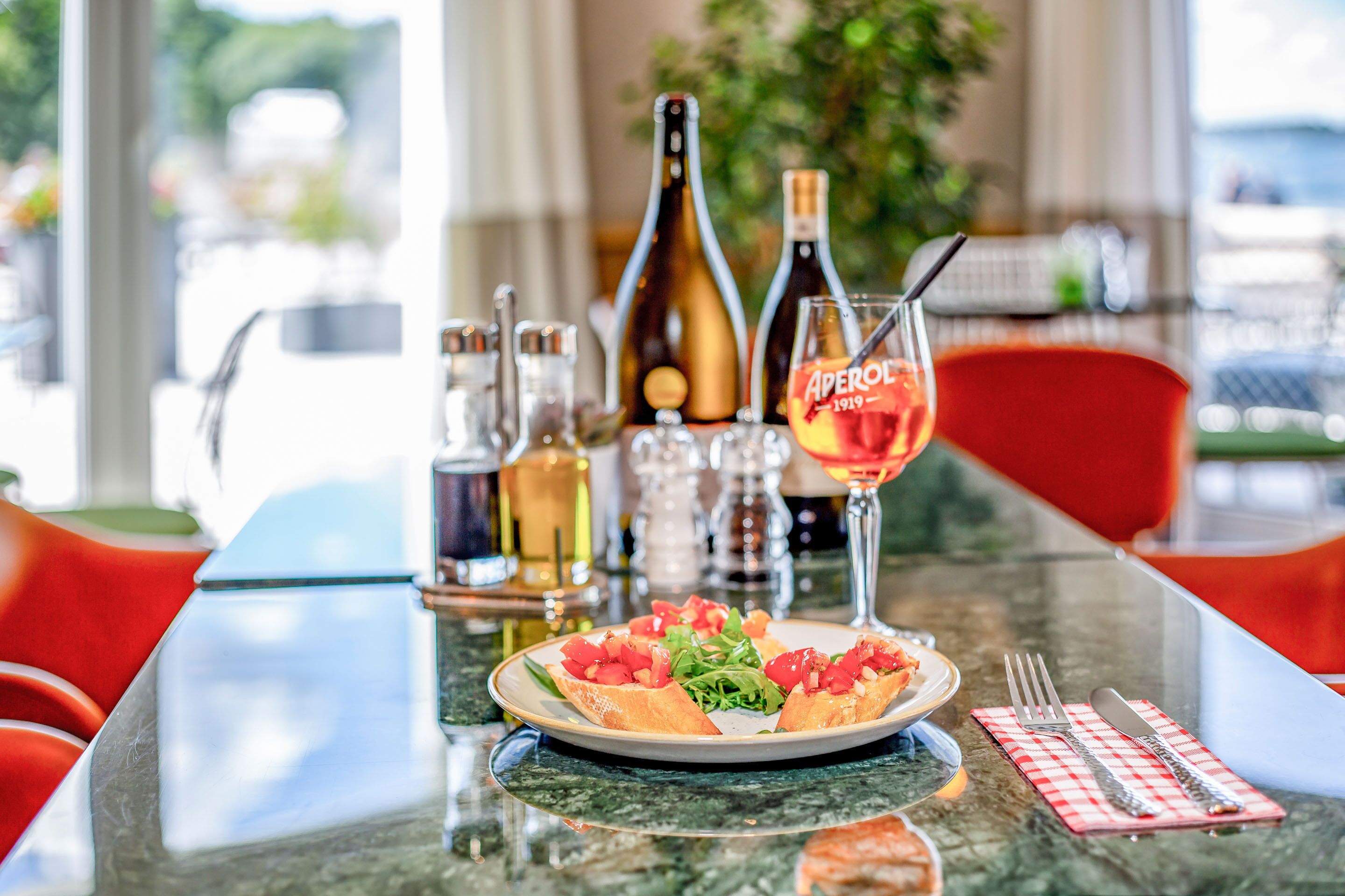 Un tavolo con un piatto di cibo, una bottiglia di Aperol e un bicchiere di vino.