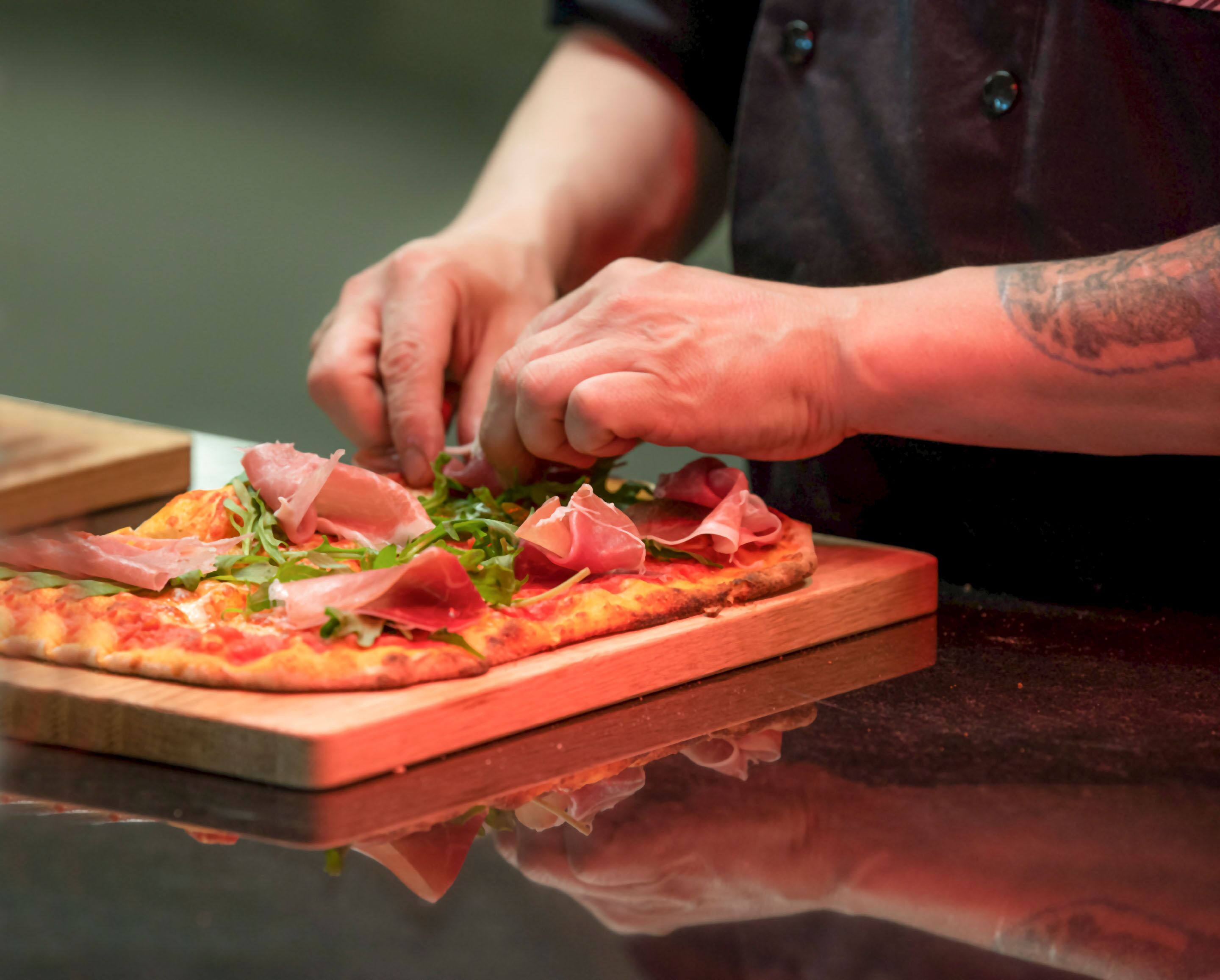 A person preparing a pizza with various toppings on a wooden board.