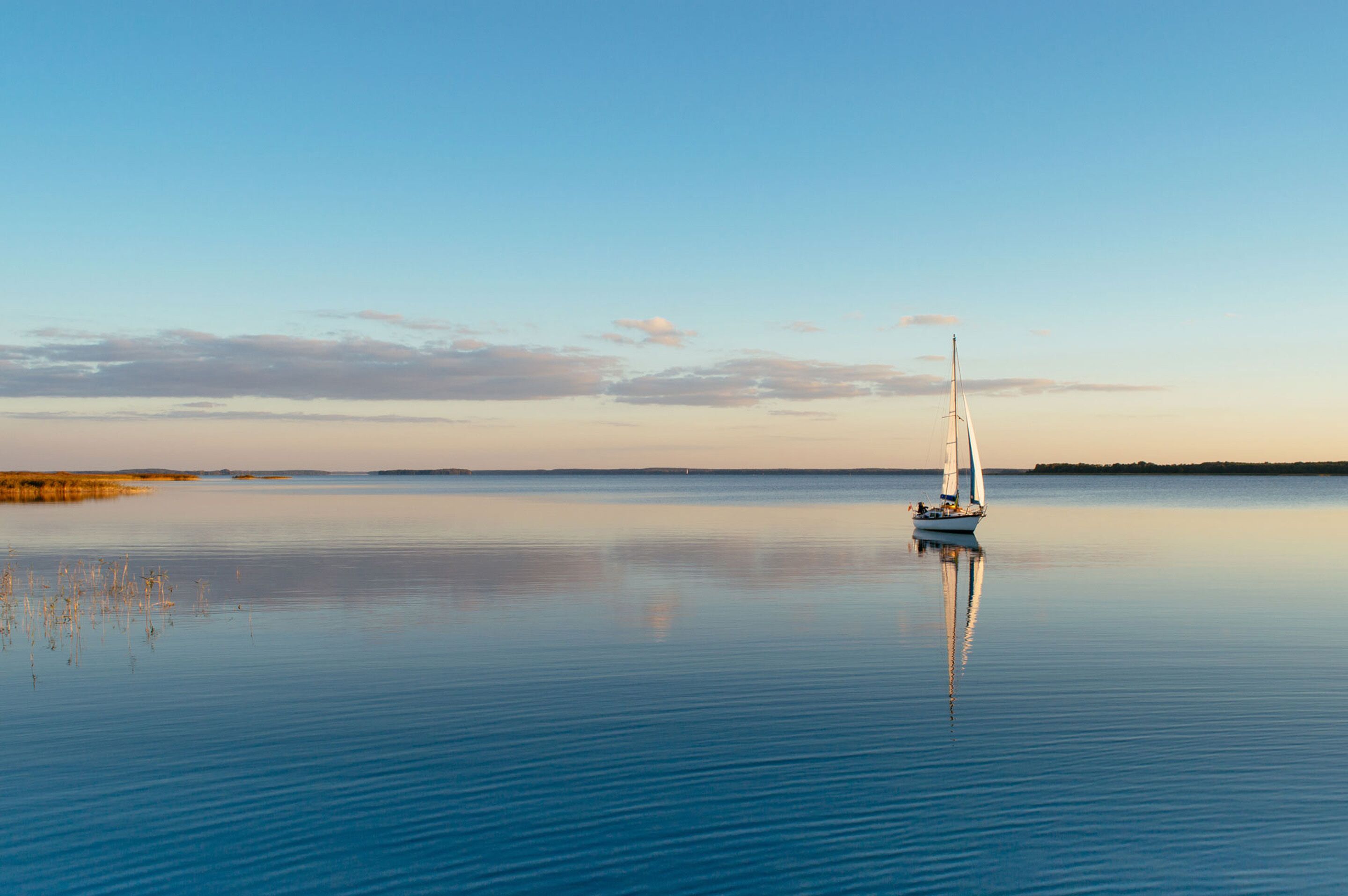 Une étendue d’eau calme, avec un voilier à l’horizon.