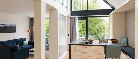 A modern kitchen with a large window, a dining area with a bench, and a living room with a sofa.