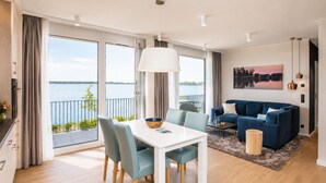 A modern living room with a dining area, a sofa, and a view of a lake. - Maremüritz Yachthafen Resort (Waren (Müritz))