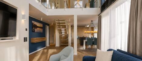 Una sala moderna con un sofá, un sillón y una escalera que lleva a un balcón.