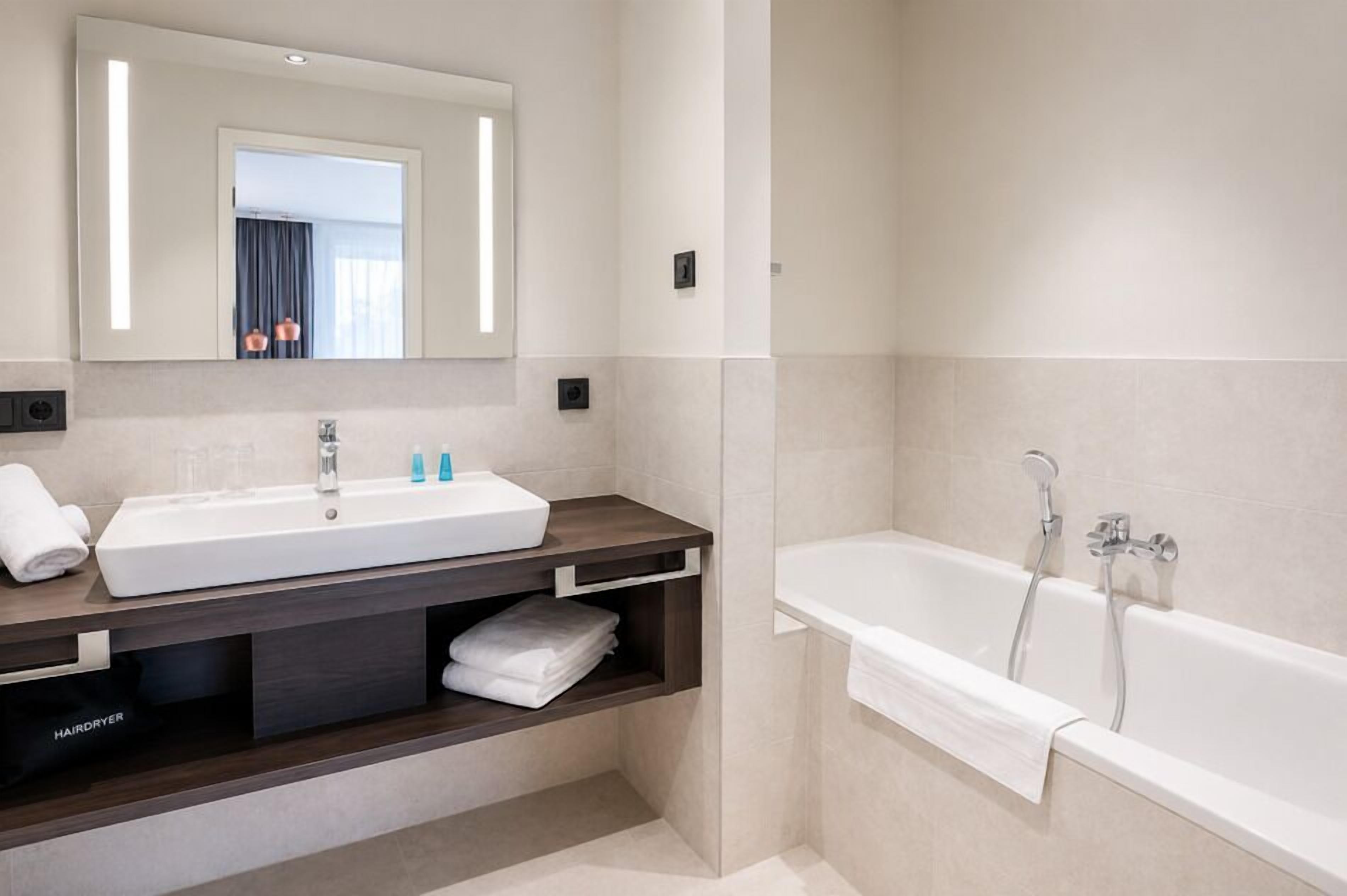 Een moderne badkamer met een grote spiegel, twee wastafels, een bad en een haardroger op het aanrecht.