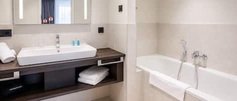 Een moderne badkamer met een grote spiegel, twee wastafels, een bad en een haardroger op het aanrecht.